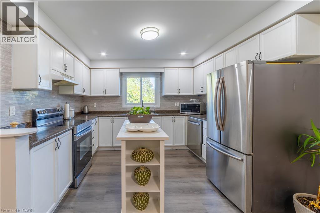 Modern kitchen featuring white cabinetry, stainless steel appliances, a dark countertop, a light-toned backsplash, and wood-finish flooring - 137 Nickolas Crescent, Cambridge, ON