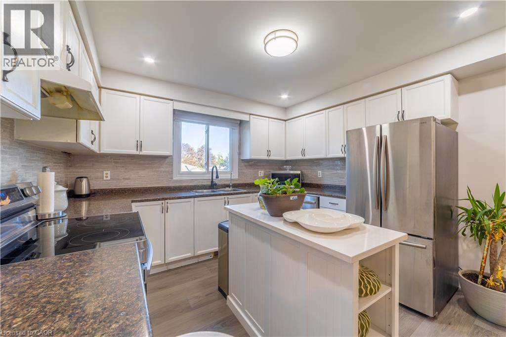 Kitchen featuring white cabinetry, dark stone-finish countertops, stainless steel appliances, a tile backsplash, and a central island with a white surface - 137 Nickolas Crescent, Cambridge, ON