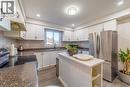 Kitchen featuring white cabinetry, dark stone-finish countertops, stainless steel appliances, a tile backsplash, and a central island with a white surface - 137 Nickolas Crescent, Cambridge, ON 