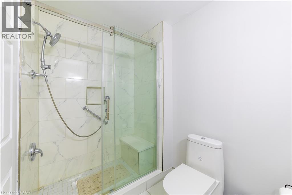 Shower with sliding glass enclosure, white tiled walls, built-in bench, and a modern toilet - 137 Nickolas Crescent, Cambridge, ON
