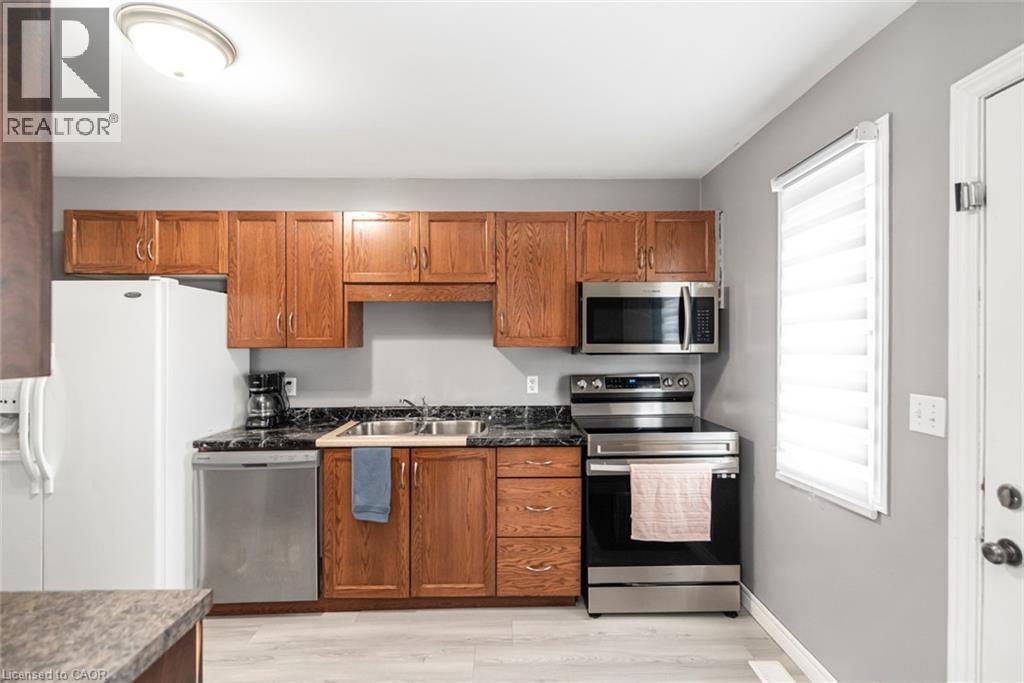 Kitchen featuring wood cabinetry, stainless steel appliances, a double basin sink, and wood-finish flooring - 42 Saturn Road, Port Colborne, ON