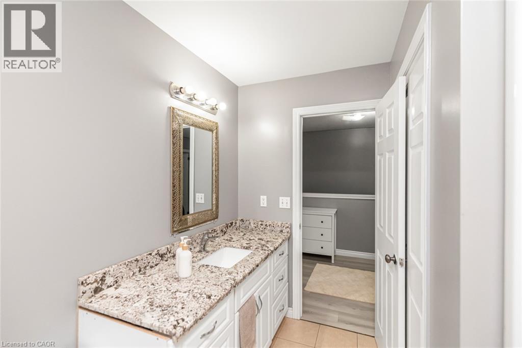Vanity with an integrated sink, granite countertop, white cabinetry, and brushed nickel light fixture - 42 Saturn Road, Port Colborne, ON
