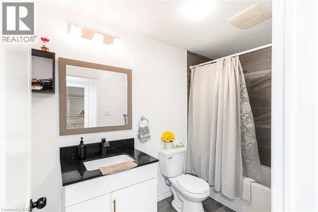 Bathroom with dark speckled countertop, white vanity, black faucet, framed mirror, and a tiled shower surround - 42 Saturn Road, Port Colborne, ON
