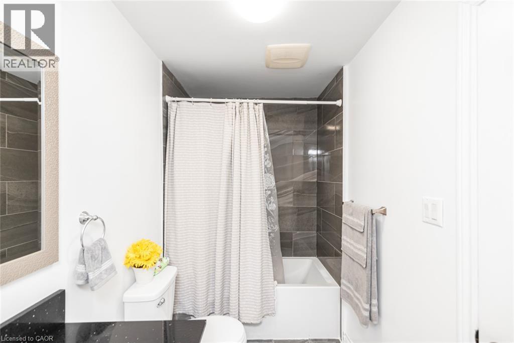 Bathroom featuring a white bathtub, dark-toned wall tiling, white toilet, and a vanity with a dark countertop - 42 Saturn Road, Port Colborne, ON