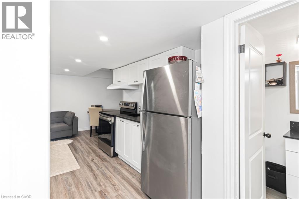 Full-size stainless steel refrigerator, white cabinetry, dark countertops, wood-finish flooring, and recessed lighting - 42 Saturn Road, Port Colborne, ON