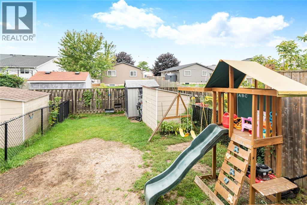 Fenced backyard with a wooden playset featuring a slide and swings, alongside a storage shed - 42 Saturn Road, Port Colborne, ON