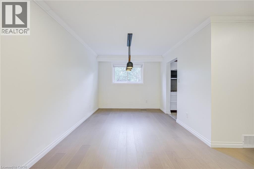 Spacious room featuring wood-finish flooring, a window, crown molding, and a modern pendant light fixture - 3148 Terraview Court, Burlington, ON