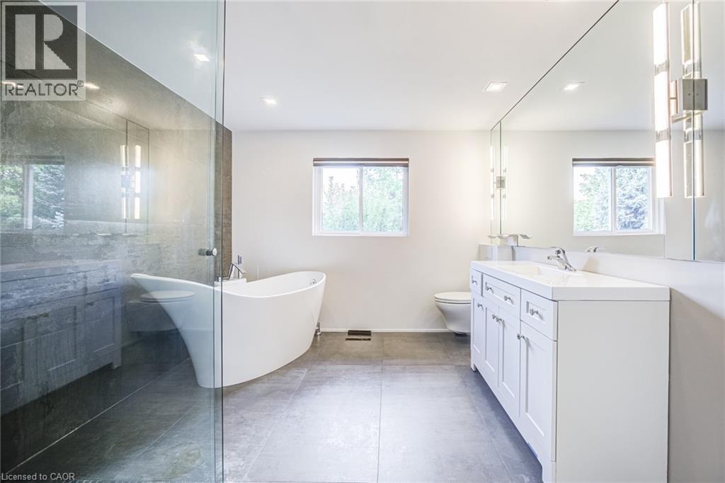 Freestanding soaking tub, frameless glass shower enclosure, double vanity with white cabinetry, integrated double sinks, and large wall-mounted mirror - 3148 Terraview Court, Burlington, ON