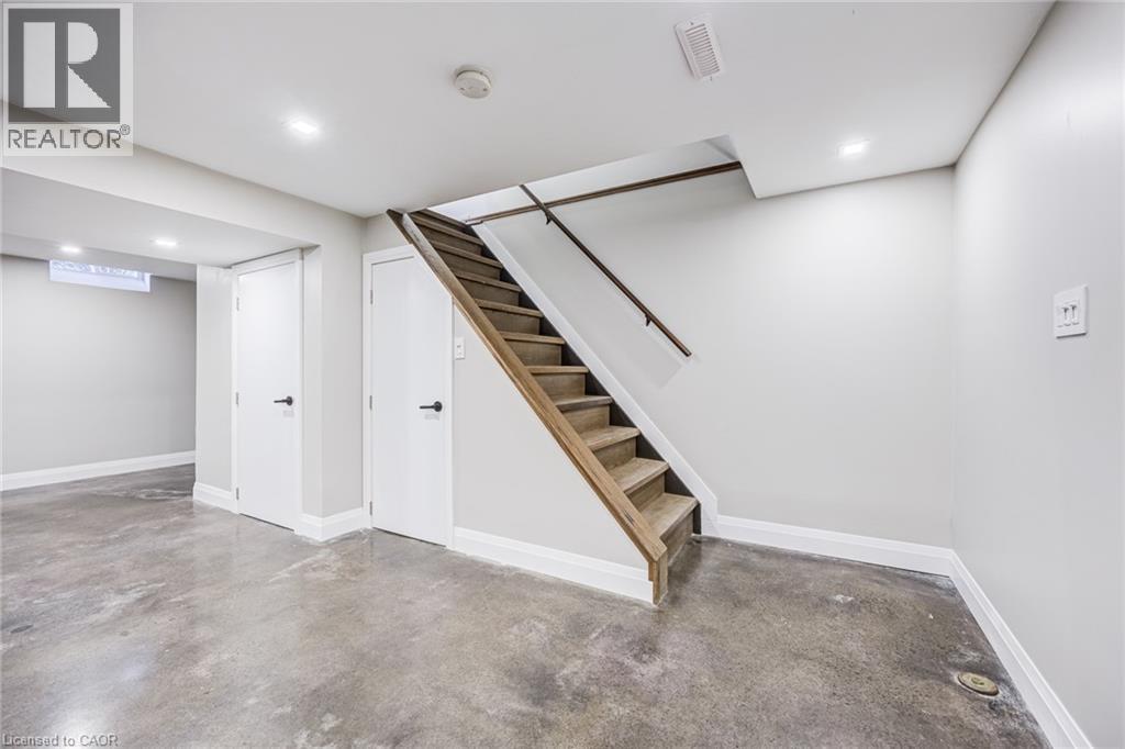 Concrete flooring, recessed lighting, white doors with matte black hardware, and wood-finish stairs with railing - 3148 Terraview Court, Burlington, ON