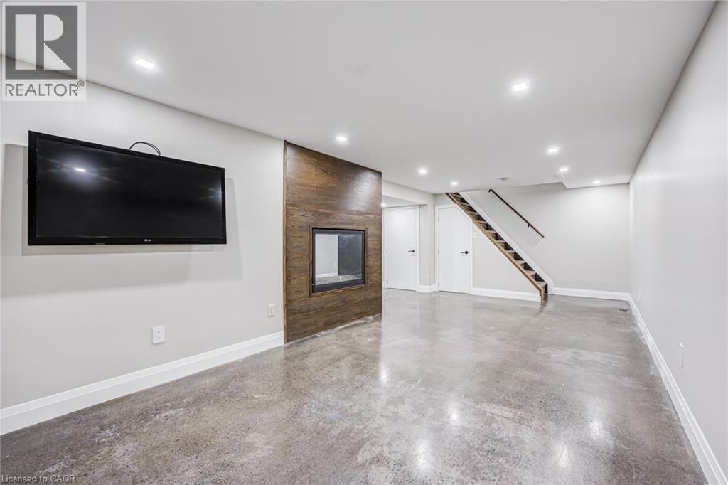 Polished concrete flooring, recessed lighting, and a modern fireplace with a wood-finish surround - 3148 Terraview Court, Burlington, ON