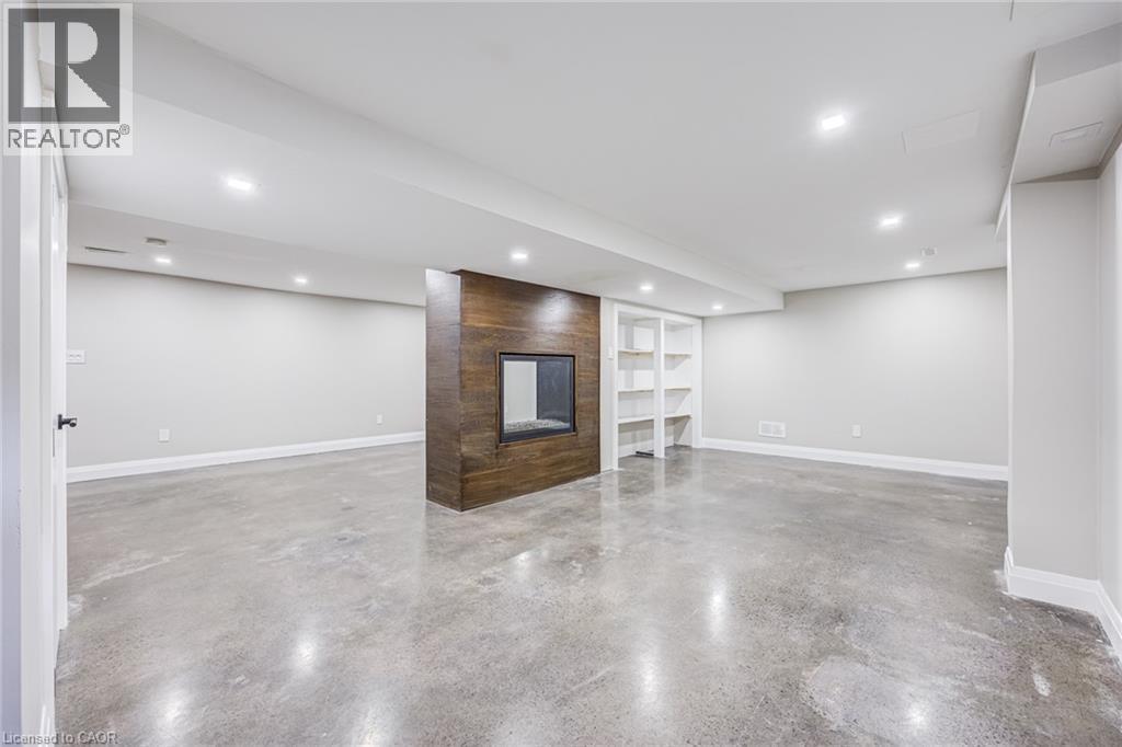 Spacious interior featuring concrete flooring, a fireplace with a wood-finish surround, built-in shelving, recessed lighting, and white baseboards - 3148 Terraview Court, Burlington, ON