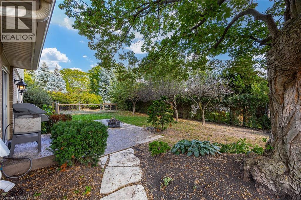 Expansive rear yard with mature trees, established plantings, a paved patio, and a stone pathway - 3148 Terraview Court, Burlington, ON
