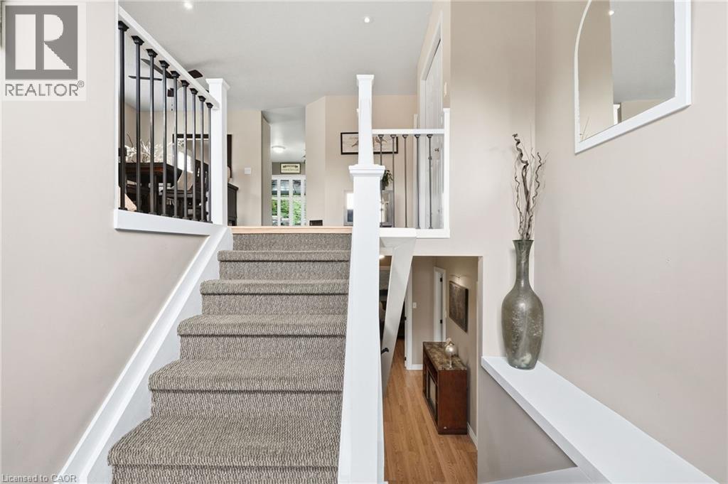 Carpeted staircase with white risers, black metal balusters, and wood-finish flooring - 94 Kent Road, Brantford, ON