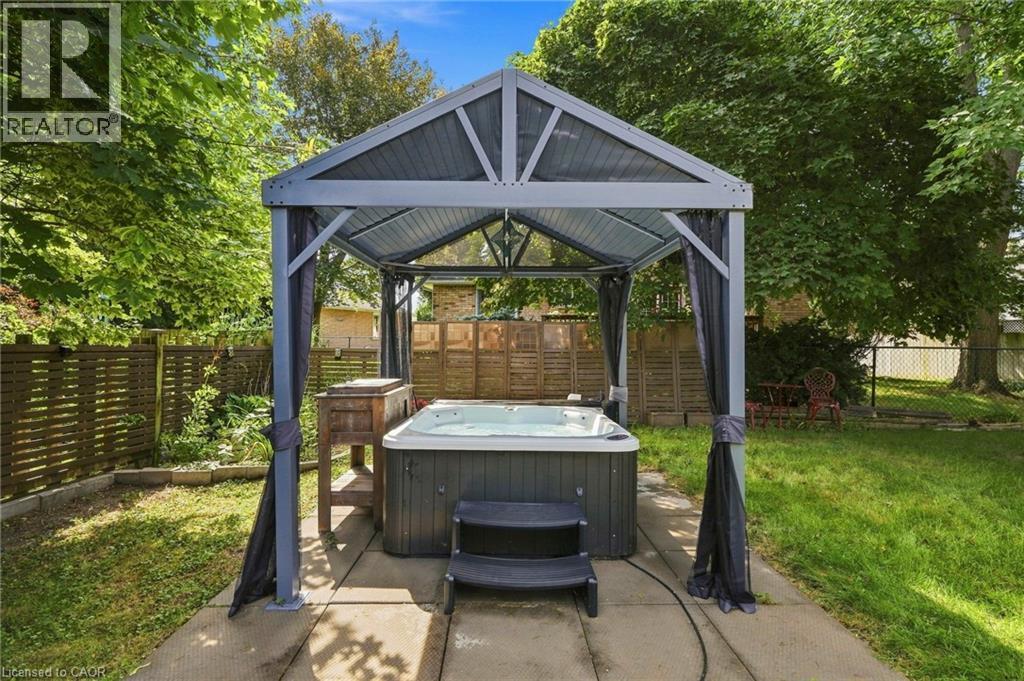 Outdoor hot tub with a protective gazebo, paved patio area, and surrounding green space with mature trees - 94 Kent Road, Brantford, ON