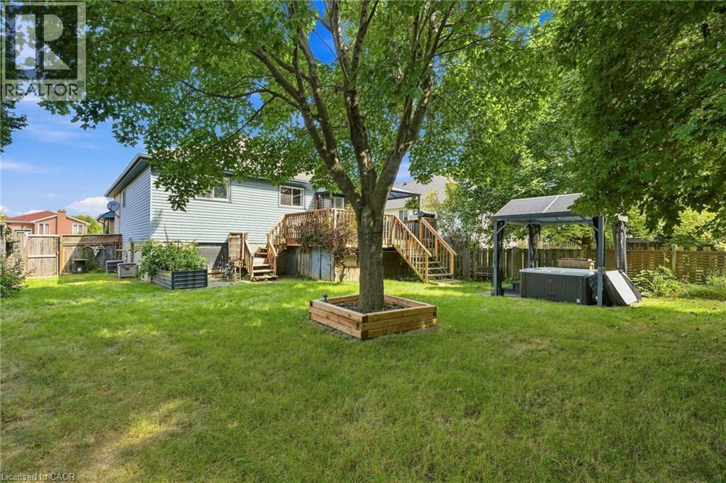 Expansive green lawn with mature trees, raised garden beds, and a multi-level wood deck - 94 Kent Road, Brantford, ON