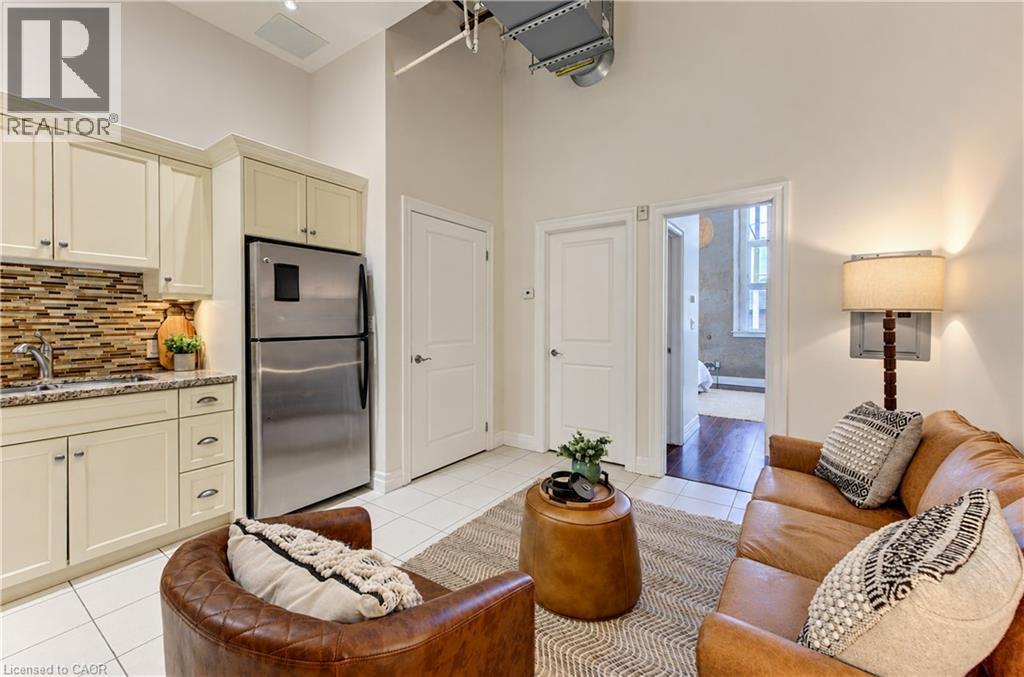 Kitchenette with cream cabinetry, stainless steel refrigerator, and tiled backsplash - 25 Concession Street Unit# 110, Cambridge, ON
