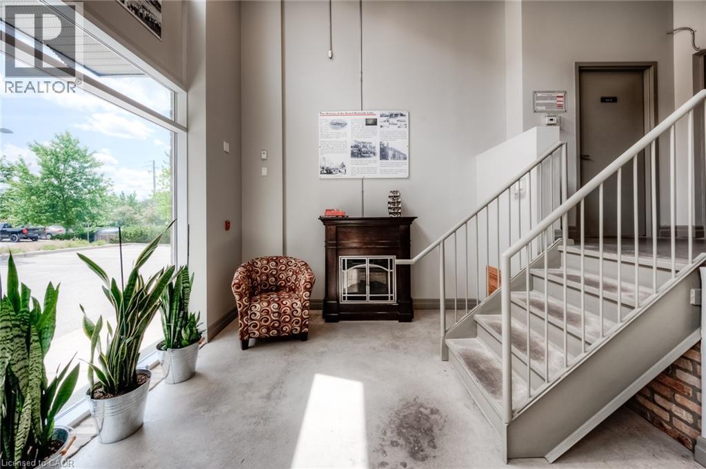Full-height windows, concrete flooring, exposed brick detailing, and a metal staircase with railing - 25 Concession Street Unit# 110, Cambridge, ON
