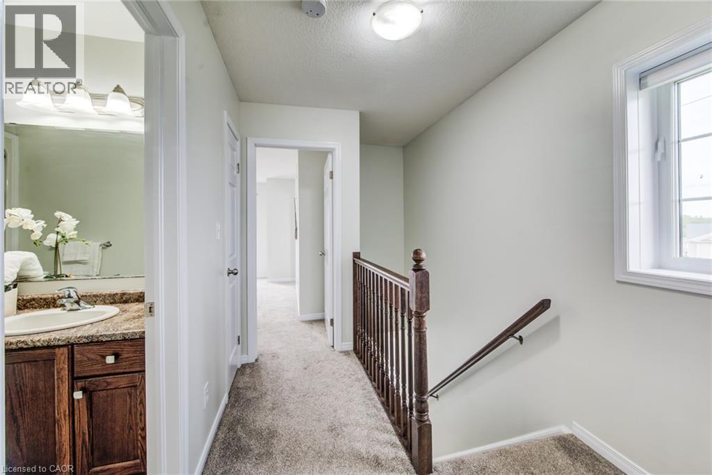 Carpeted hallway with a window, a wooden handrail, and a bathroom entry featuring a vanity with a sink - 226 Maitland Street, Kitchener, ON