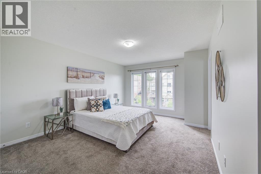 Carpeted bedroom featuring three expansive windows, a textured upholstered headboard, and a flush-mount ceiling light - 226 Maitland Street, Kitchener, ON