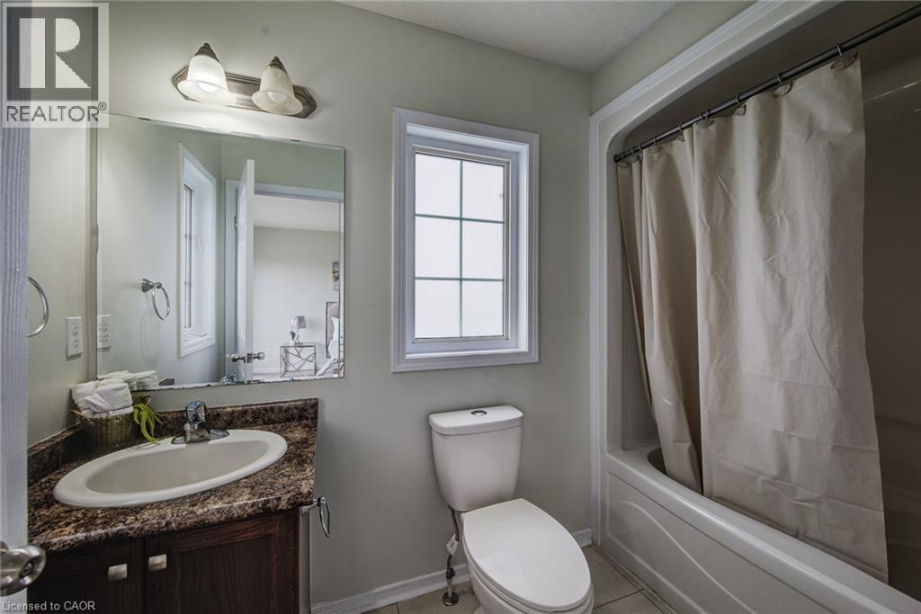 Bathroom featuring a single vanity with an oval sink, a wall-mounted mirror, a window with grid patterns, and a tub with a shower - 226 Maitland Street, Kitchener, ON