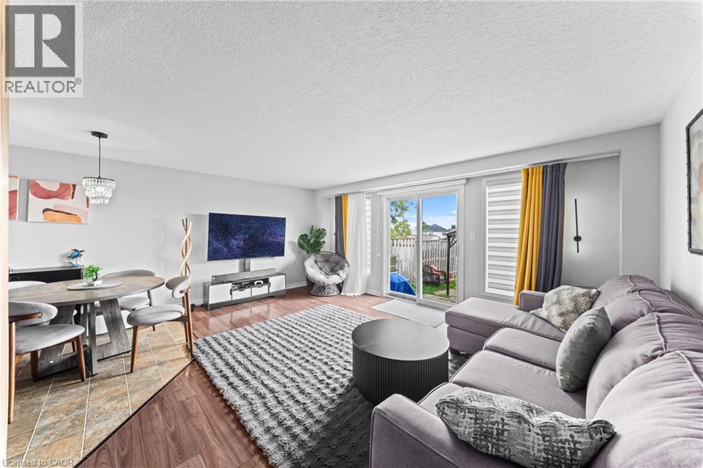 Open-concept living area with wood-finish flooring, a sliding glass door to the backyard, and a dining area featuring a chandelier - 245 Red Clover Court, Kitchener, ON