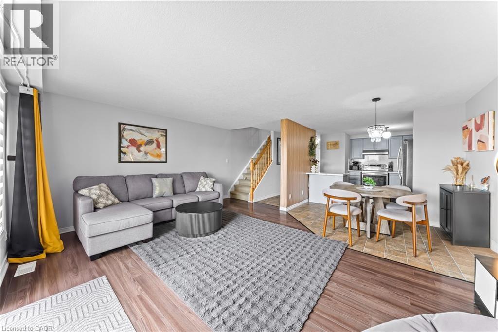 Wood-finish flooring, staircase with wood railings, kitchen with stainless steel appliances, and a dining area with pendant lighting - 245 Red Clover Court, Kitchener, ON