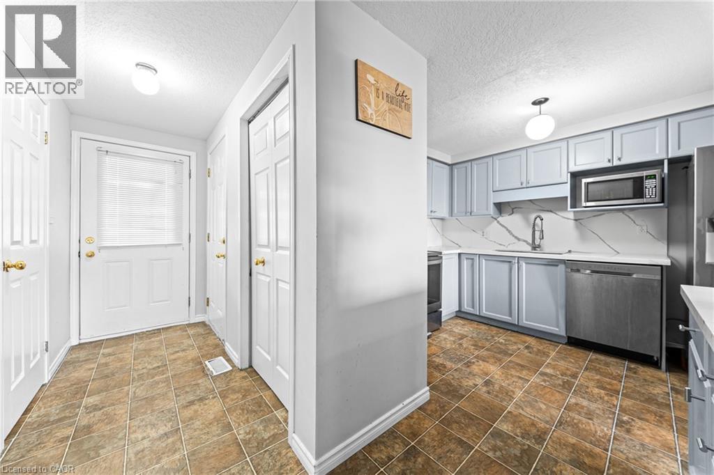 Kitchen featuring light blue cabinetry, white countertops, stainless steel appliances, and a white backsplash with gray veining - 245 Red Clover Court, Kitchener, ON