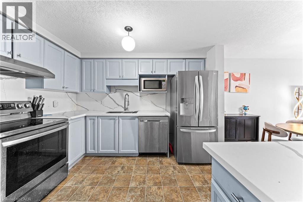 Kitchen featuring light blue cabinetry, white countertops with veining, stainless steel appliances, and a tile floor - 245 Red Clover Court, Kitchener, ON