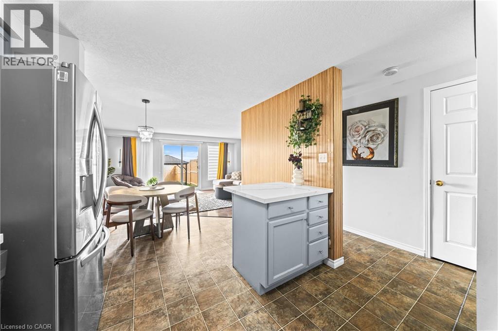 Tile flooring, stainless steel refrigerator, kitchen island with storage, wood slat accent wall, sliding glass doors - 245 Red Clover Court, Kitchener, ON