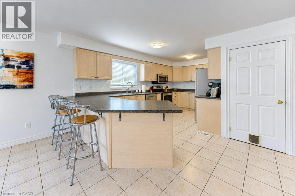 Kitchen featuring light wood-finish cabinetry, dark countertops, and stainless steel appliances - 88 Decaro Crescent, Cambridge, ON