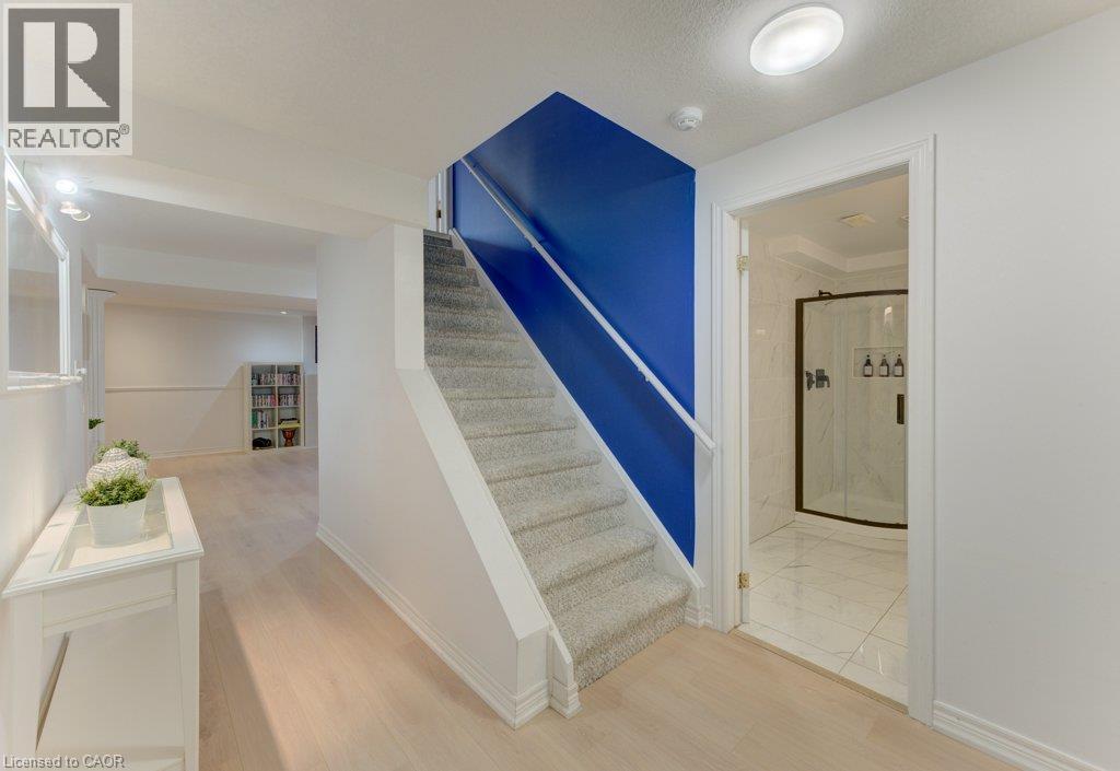 Carpeted staircase with contrasting accent wall, light wood-finish flooring, and a bathroom featuring a corner glass-enclosed shower with dark trim - 88 Decaro Crescent, Cambridge, ON