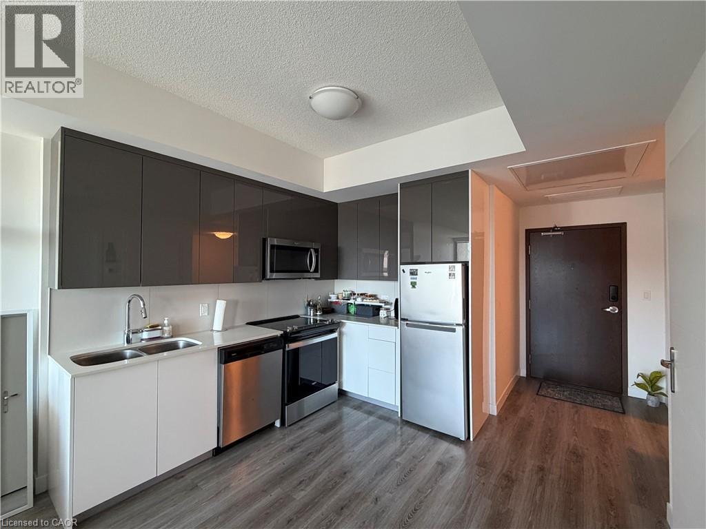 Modern kitchen featuring sleek gray upper cabinetry, white lower cabinetry, stainless steel appliances, wood-finish flooring, and a white backsplash - 60 Frederick Street Unit# 1213, Kitchener, ON