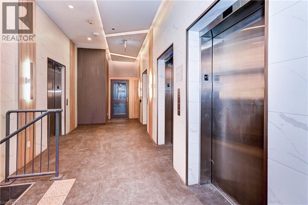 Elevator lobby featuring multiple stainless steel elevator doors, recessed ceiling lighting, wall-mounted sconces, and wood-finish wall panels - 60 Frederick Street Unit# 1213, Kitchener, ON