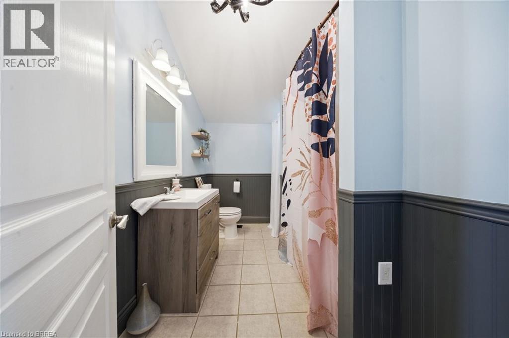Bathroom featuring a wood-finish vanity with an integrated sink, a large wall mirror, and a three-light vanity fixture - 62 East Avenue, Brantford, ON