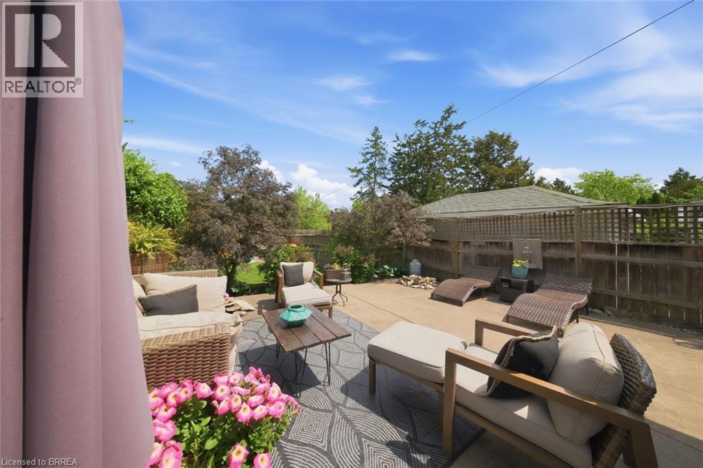 Spacious concrete patio featuring a decorative outdoor rug, perimeter fencing, and mature landscaping - 62 East Avenue, Brantford, ON