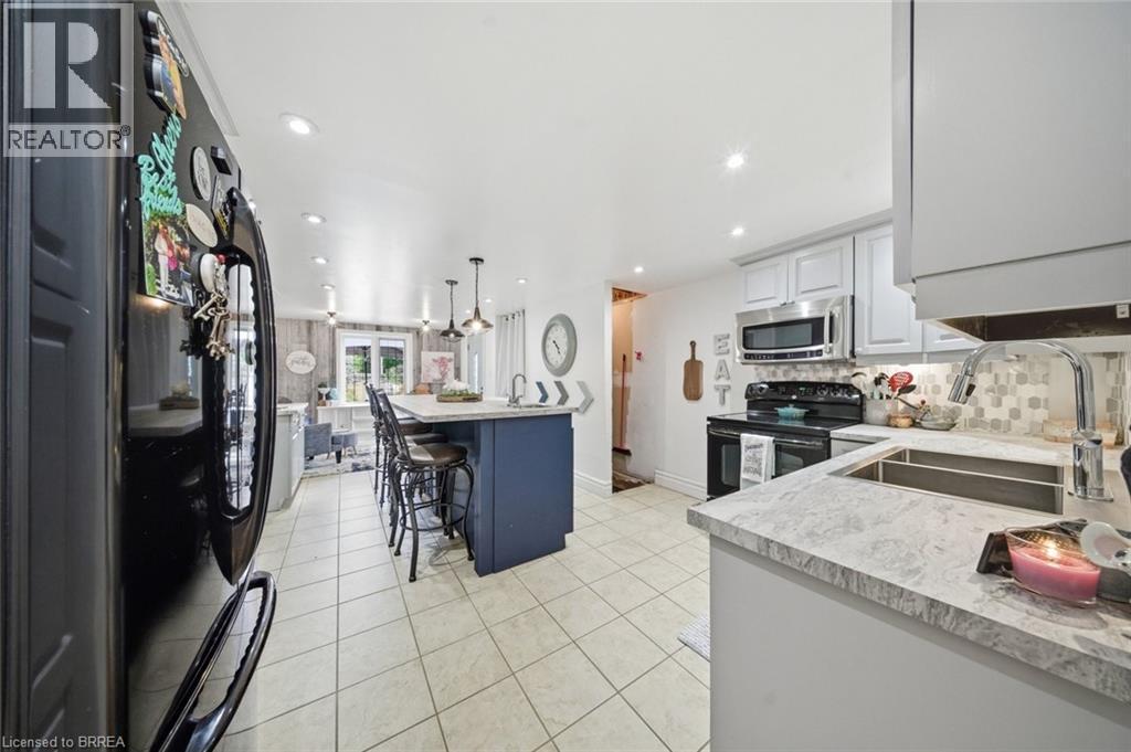 Bright kitchen featuring a central island with seating, pendant lighting, stainless steel appliances, light cabinetry, and tiled flooring - 62 East Avenue, Brantford, ON