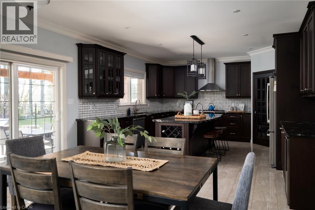 Spacious kitchen featuring dark wood cabinetry, dark countertops, a tiled backsplash, stainless steel appliances, and a central island with integrated wine storage - 1505 Milburough Line, Carlisle, ON