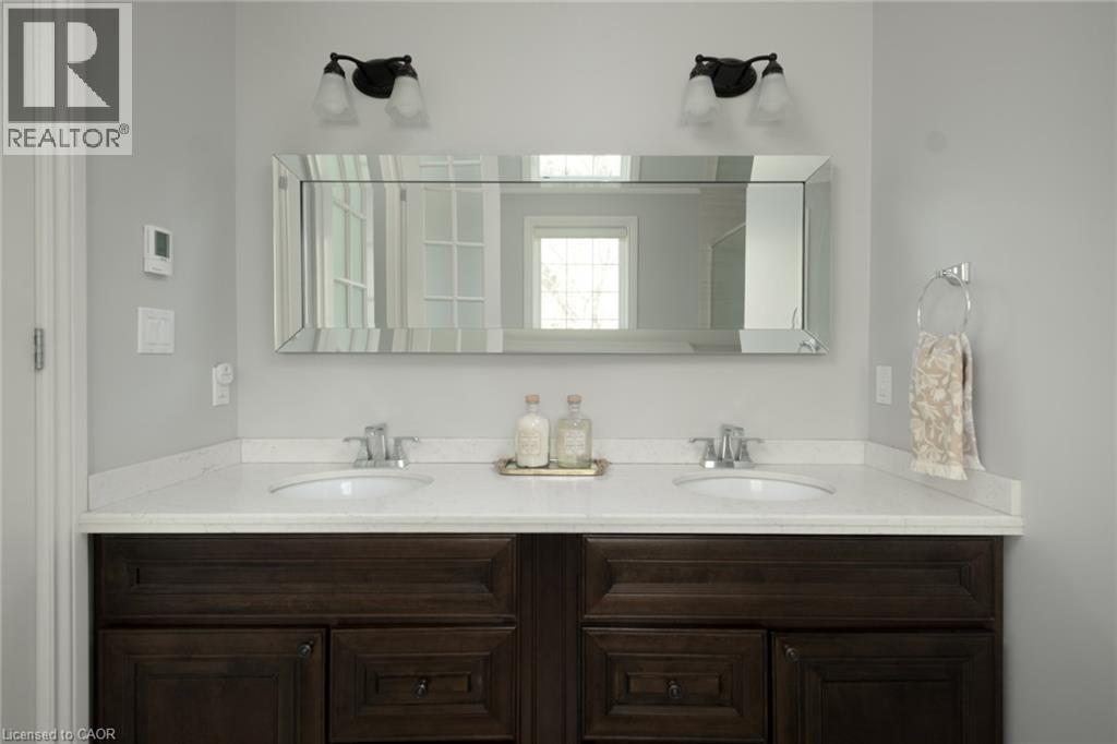 Dual vanities with undermount sinks, white solid-surface countertop, dark wood-finish cabinetry, and a beveled mirror - 1505 Milburough Line, Carlisle, ON