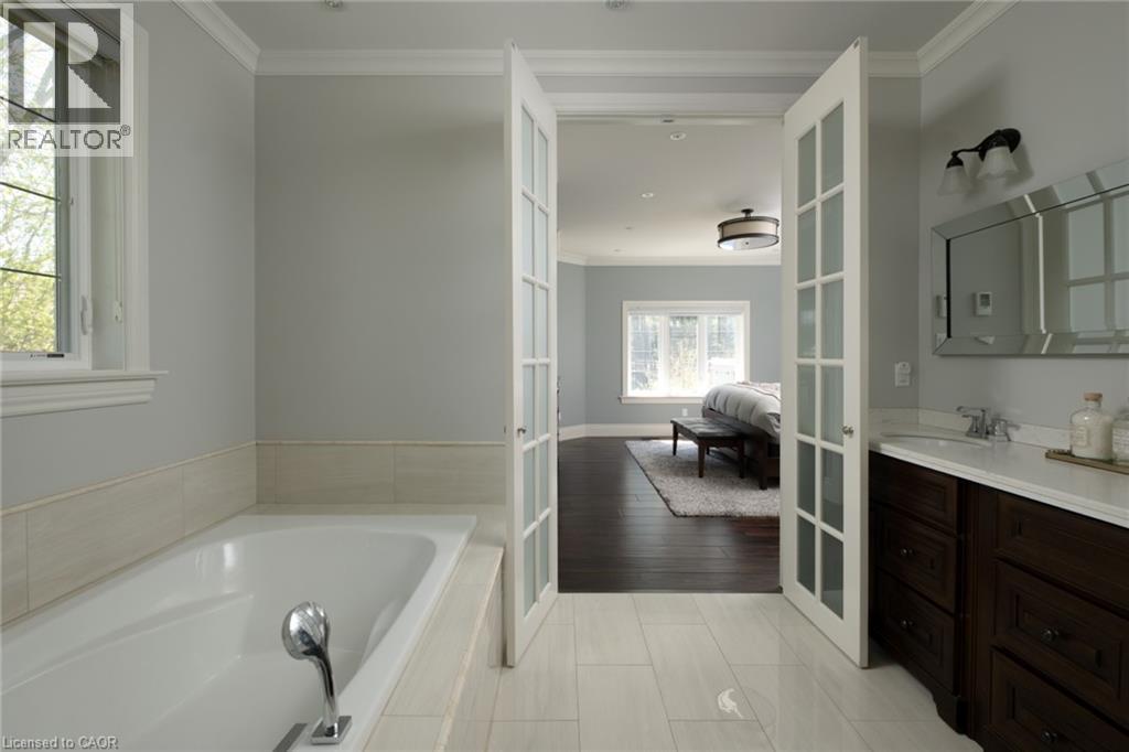 Soaking tub with chrome fixtures, light-toned tile flooring, dark wood-finish vanity with a white countertop, and framed vanity mirror - 1505 Milburough Line, Carlisle, ON