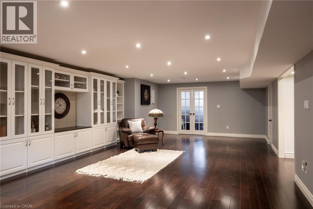 Dark wood-finish flooring, recessed lighting, expansive white built-in cabinetry with glass fronts, a built-in counter, and double French doors - 1505 Milburough Line, Carlisle, ON