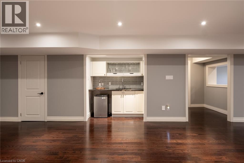 Dark wood-finish flooring, recessed lighting, and a wet bar featuring white cabinetry, a dark countertop, and a tiled backsplash - 1505 Milburough Line, Carlisle, ON