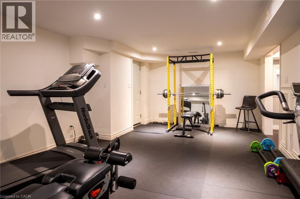 Recessed lighting illuminates the space, featuring a full-height yellow power rack, rubber floor tiles, and a white paneled door - 1505 Milburough Line, Carlisle, ON