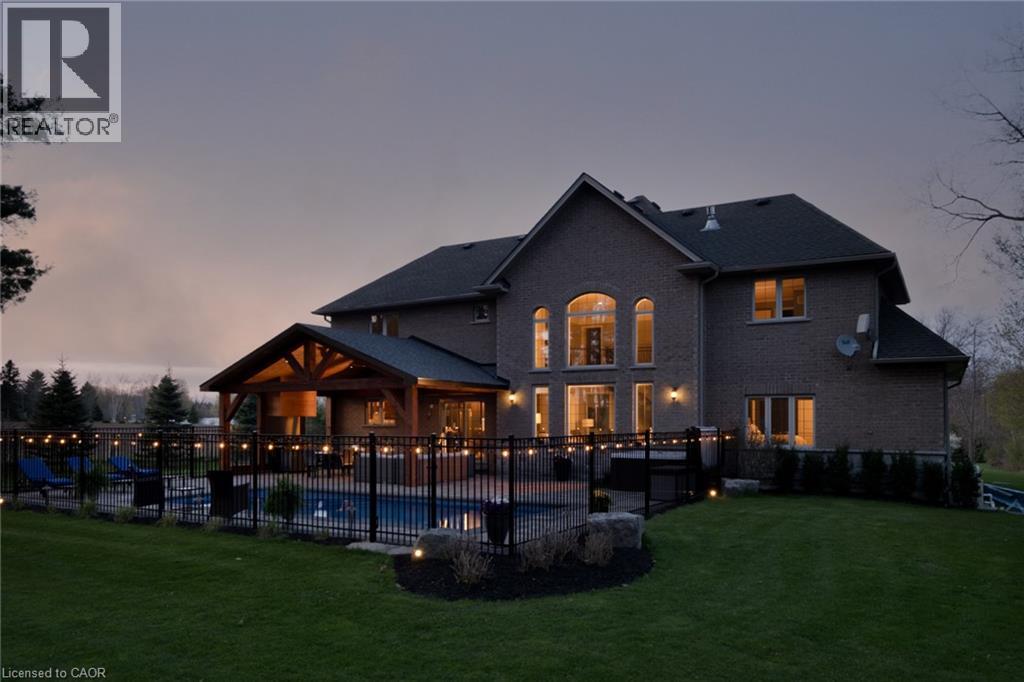 Brick exterior with a gabled roofline, multiple arched windows, and an outdoor swimming pool - 1505 Milburough Line, Carlisle, ON