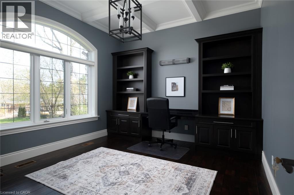 Arched window, dark wood-finish flooring, coffered ceiling, built-in shelving, and a modern chandelier - 1505 Milburough Line, Carlisle, ON