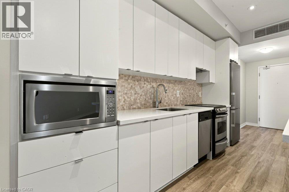 Contemporary kitchen featuring white flat-panel cabinetry, stainless steel appliances, a mosaic tile backsplash, light-toned countertops, and wood-finish flooring - 457 Plains Road Unit# 225, Burlington, ON