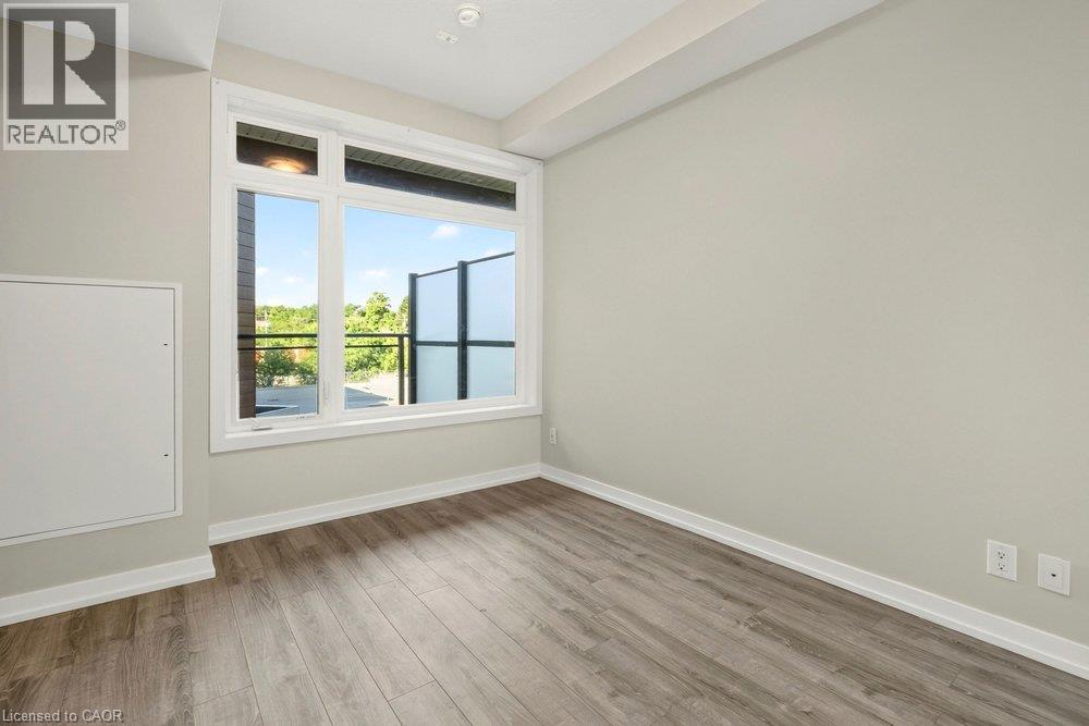Room featuring wood-finish flooring, a large window, light-colored walls, white baseboards, and a recessed ceiling light - 457 Plains Road Unit# 225, Burlington, ON