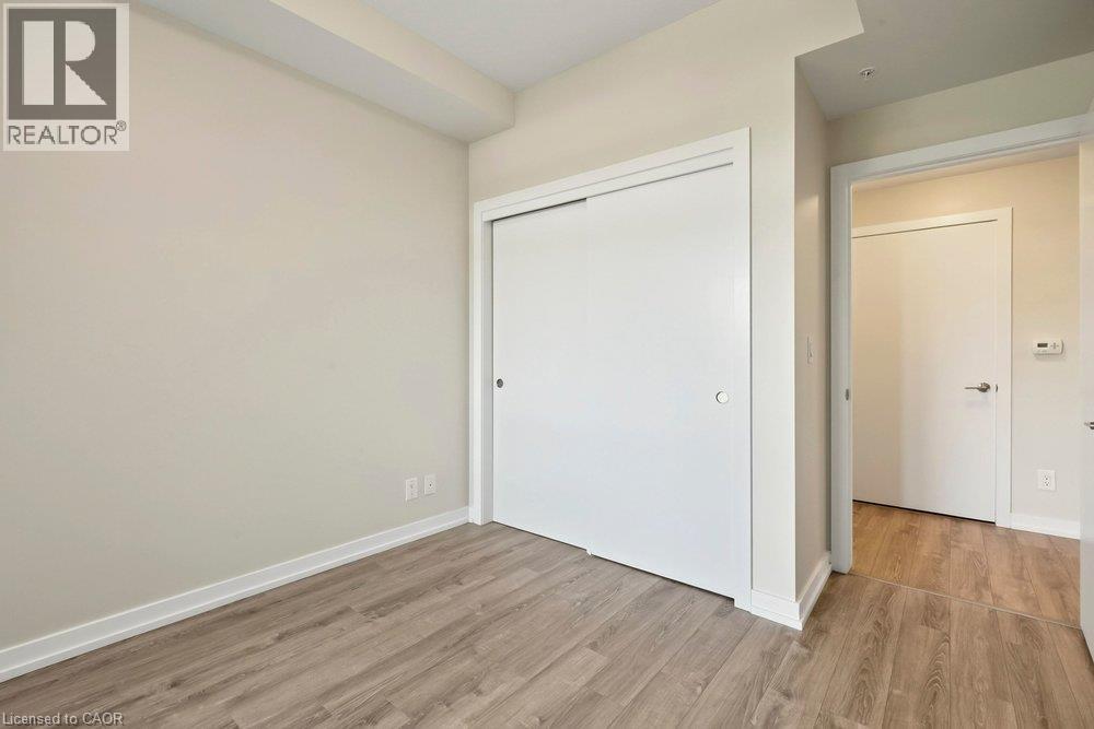 Room featuring wood-finish flooring, a sliding closet door with a circular handle, and light-toned walls - 457 Plains Road Unit# 225, Burlington, ON