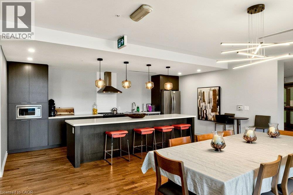 Open-concept kitchen and dining area featuring rich wood-finish flooring, dark wood-finish cabinetry, a large kitchen island with white countertop, and a modern linear chandelier - 457 Plains Road Unit# 225, Burlington, ON
