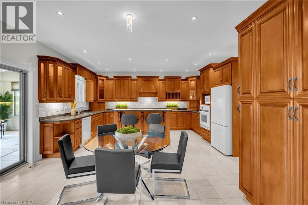Spacious kitchen featuring extensive wood cabinetry, undermount lighting, dark countertops, a tile backsplash, and a built-in oven - 302 German School Road, Paris, ON