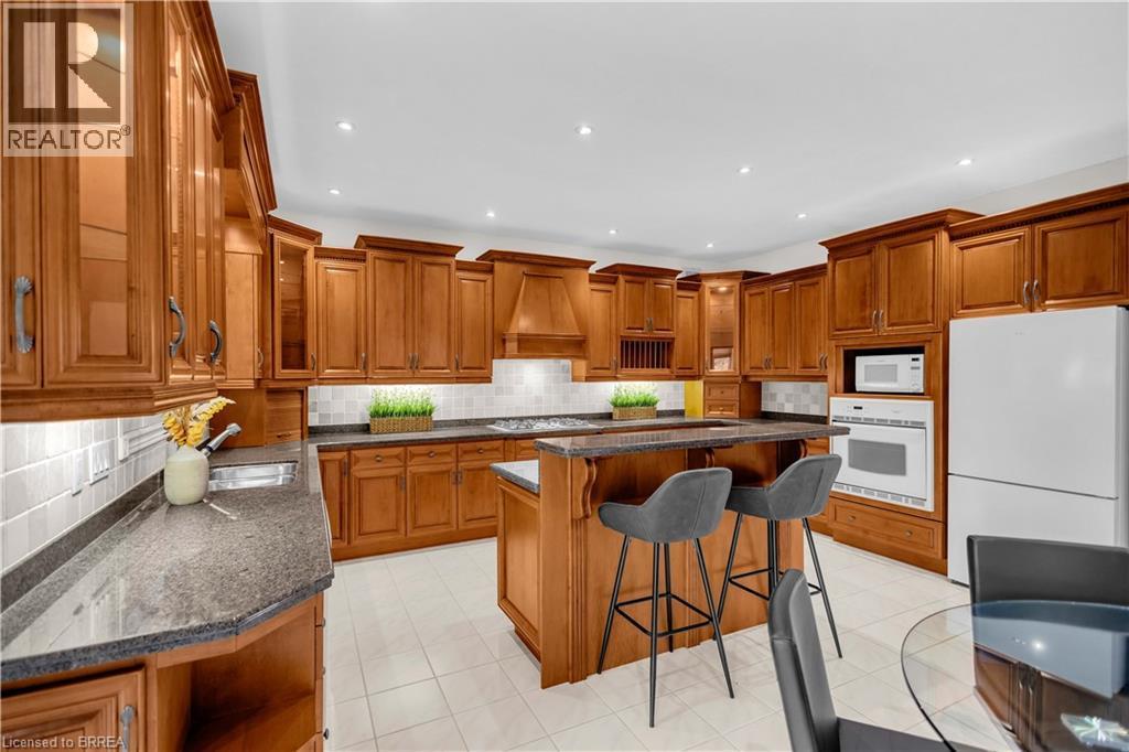 Expansive kitchen featuring custom wood cabinetry, granite countertops, white tile backsplash, a central island with bar seating, and integrated appliances - 302 German School Road, Paris, ON